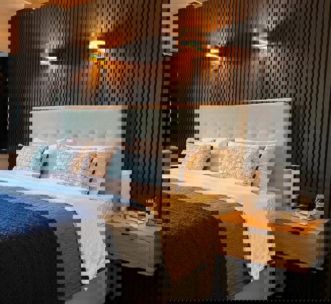 Neatly made bed with decorative pillows in a bedroom setting with Black Oak acoustic slatted panels.