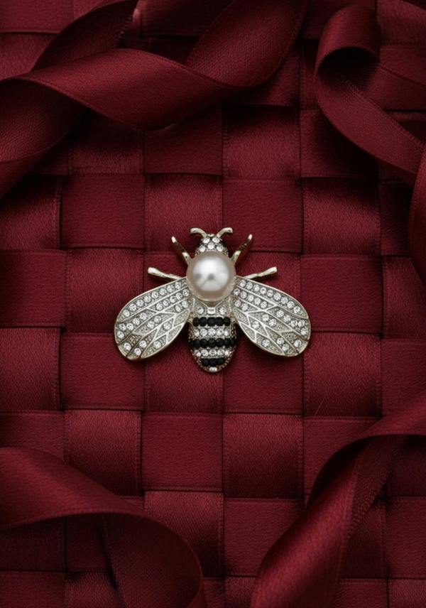Decorative bee brooch with pearl on a red textured fabric background