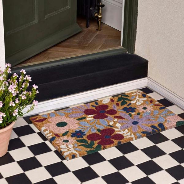 Decorative doormat with floral pattern on a checkered floor in front of a door.