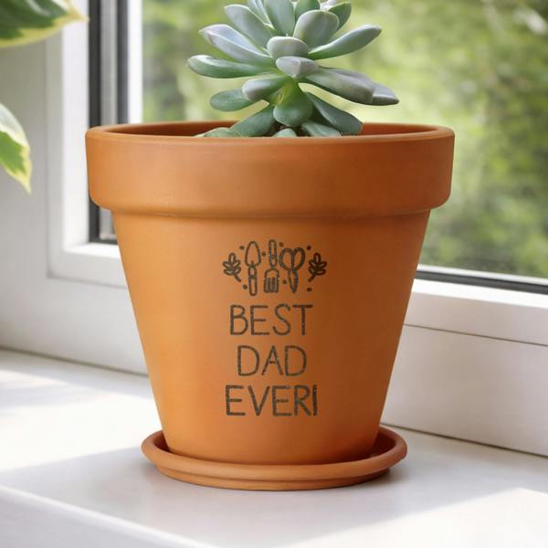 A personalised terracotta plant pot engraved with 'Best Dad Ever!' and holding a succulent, sitting on a white windowsill with a blurred green background.