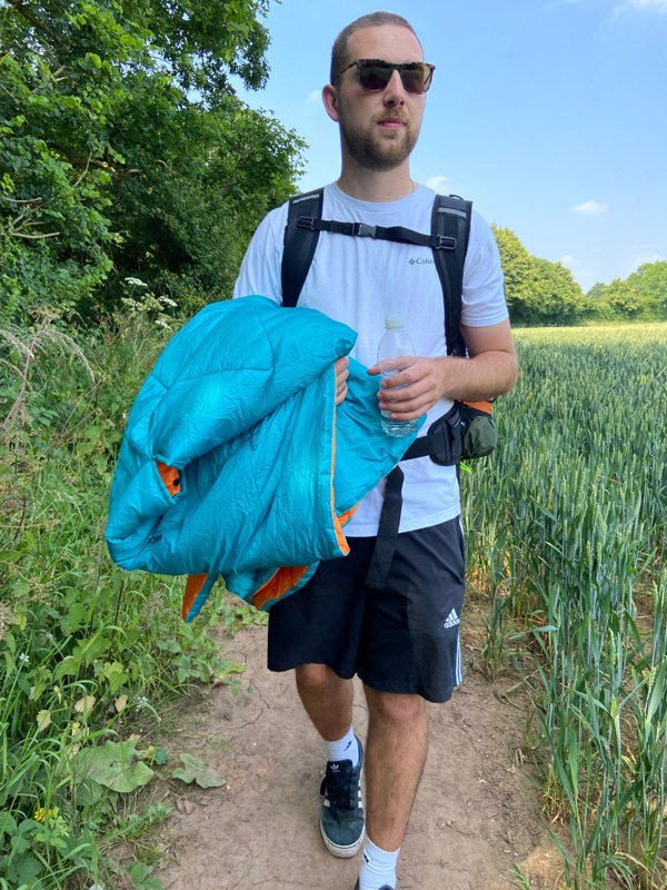 An adult carrying the OLPRO Insulated Outdoor Reversible Blanko along a dirt track in a field.