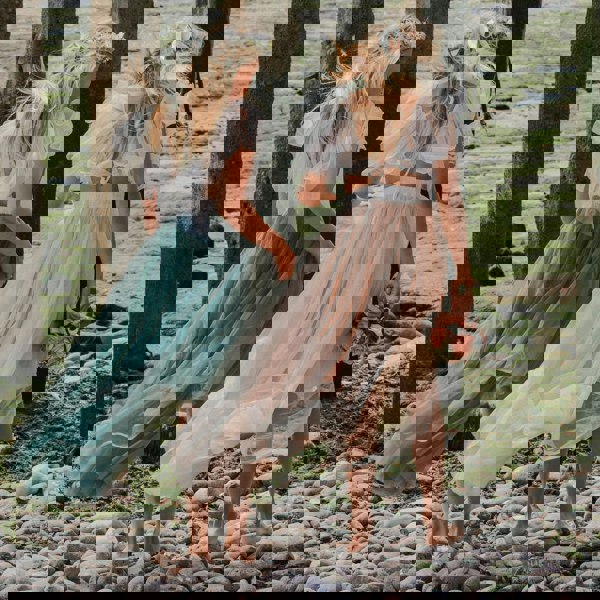 Two girls in flowing dresses walking on a rocky path on the beach