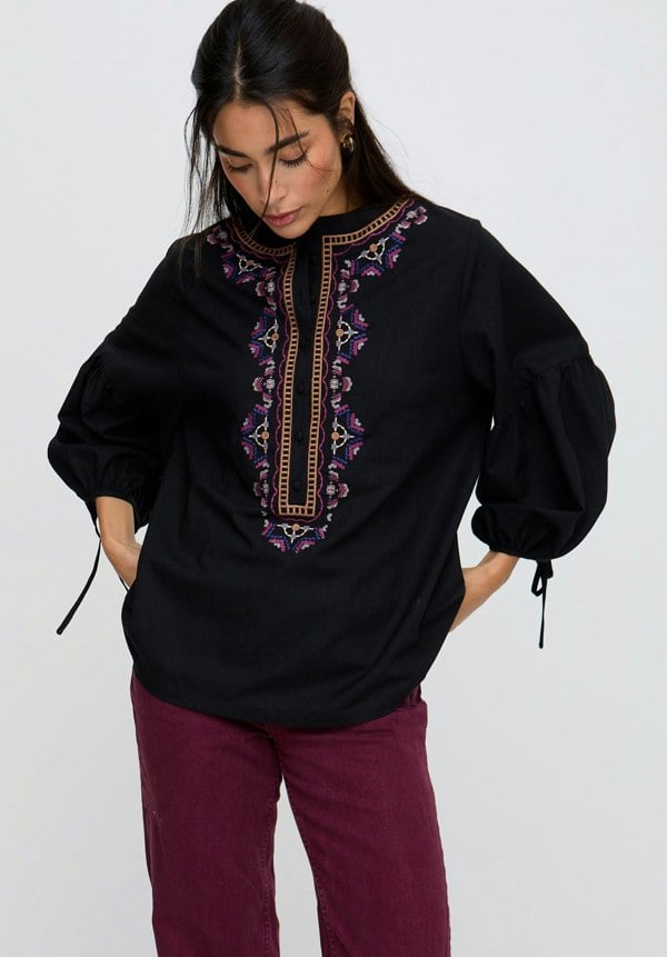 Woman wearing a black blouse with intricate embroidery on a white background