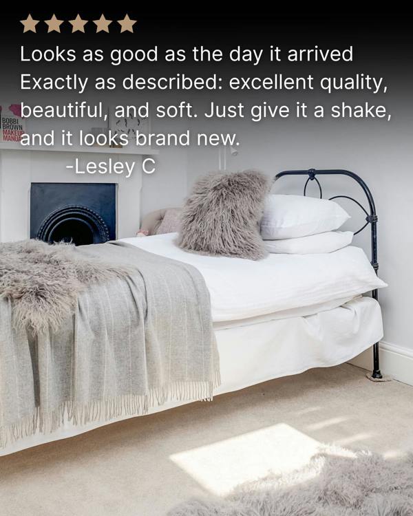 Grey mongolian sheepskin pillow on white bed with grey blanket