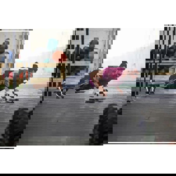 Man performing push-ups on a push-up stand in an outdoor setting with exercise balls in the background.