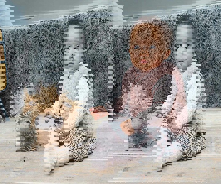 Baby girl sat next to Hubert Highland Cow Pull Along Toy with removable wooden wheels