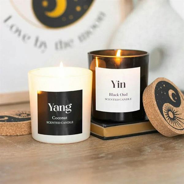Two Yin-Yang scented candles: white coconut Yang and black oud Yin, both with flames
