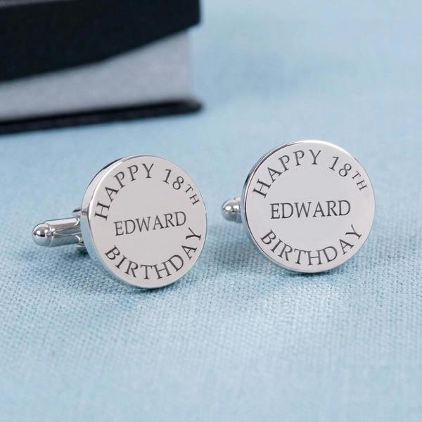 A pair of personalised rhodium-plated birthday cufflinks engraved with 'Happy 18th Edward Birthday' resting on a textured soft blue tablecloth.