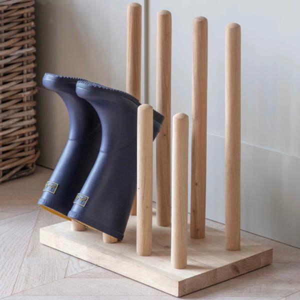 A solid oak welly stand holding various pairs of rubber wellington boots inside an entryway by Abode Home & Gifts.