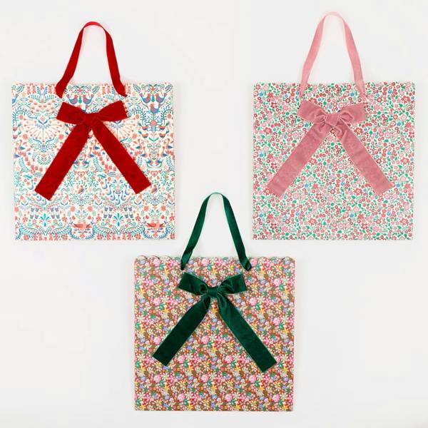 Flat-lay view of three Liberty print Christmas gift bags with red, pink, and dark green velvet handles and bows.