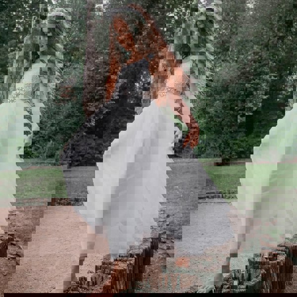 A young girl wearing a white sleeveless Bohemian style flower girl dress with a layered tulle skirt and lace detailing, standing on wooden steps.