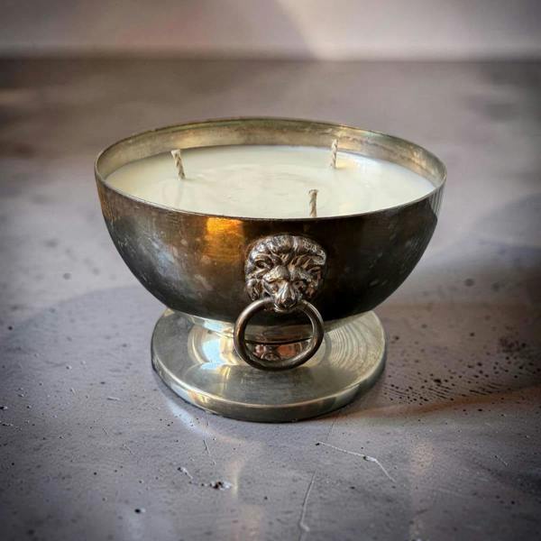 Decorative candle in a metal holder with lion head design on a metallic surface