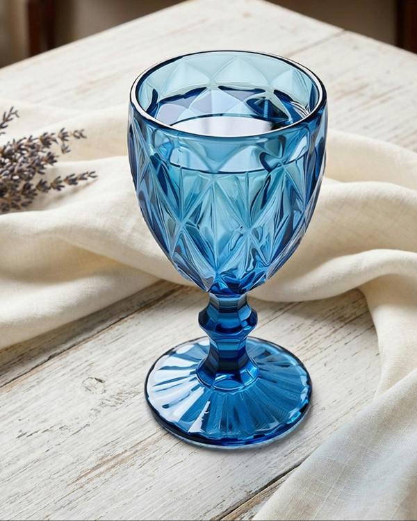 Blue glass goblet on a wooden table with a white cloth and lavender.