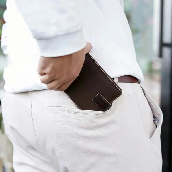 Person wearing a white shirt and light-colored pants with a brown leather wallet in their pocket.
