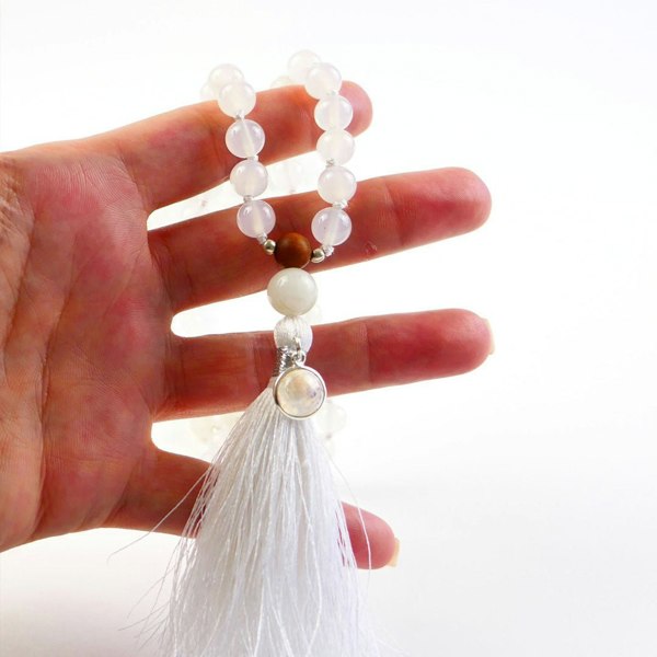 Hand holding Kati Kaia crystal moonstone mala necklace with white beads and tassel on white background