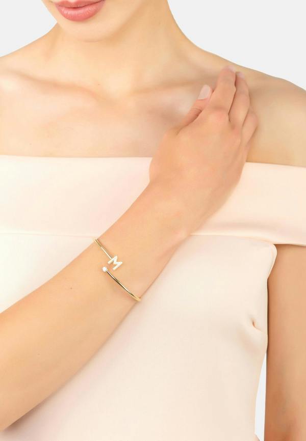 Gold bracelet with a small round charm on a person's wrist against a light background