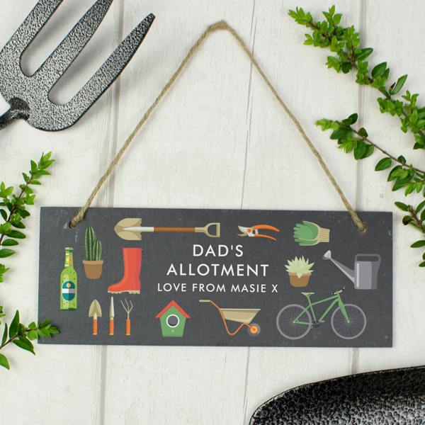 A rectangular hand-cut dark slate sign with natural string, greenhouse plant illustrations, and custom text reading nan's greenhouse plants grown with love.