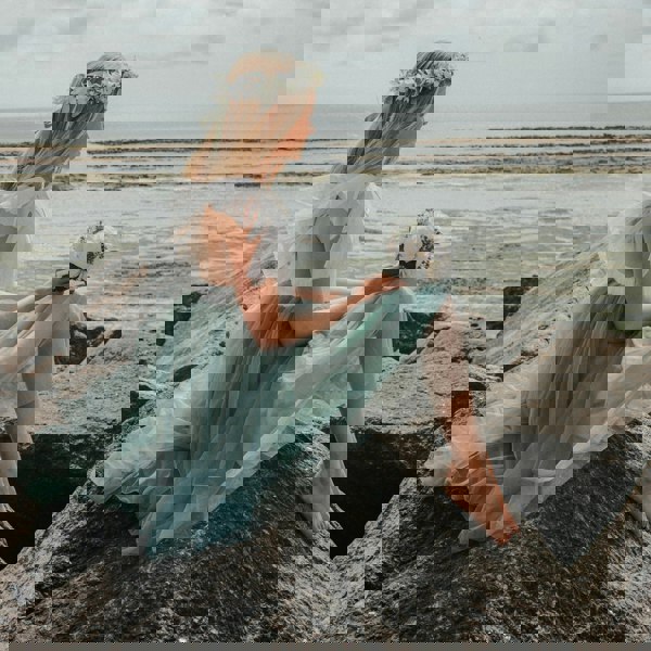 Girl in a sage coloured Bohemian Serendipity Dress sitting on a rock by the sea