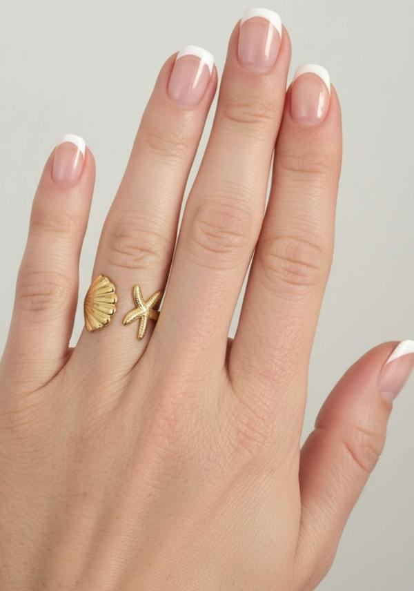 Hand wearing a gold ring with shell and starfish designs on a neutral background