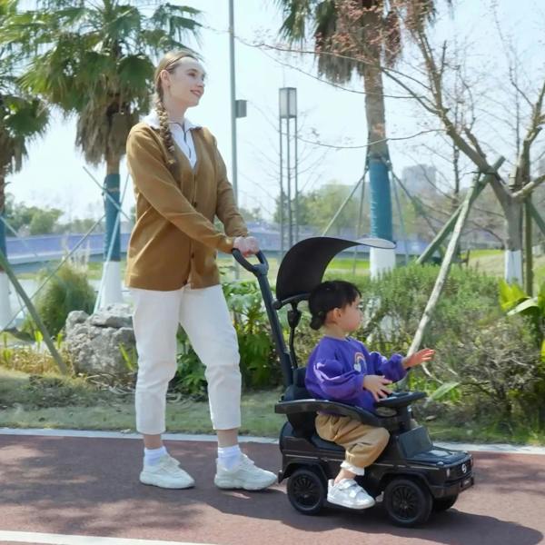 Black kids ride-on push car with seated child, pushed outdoors by an adult