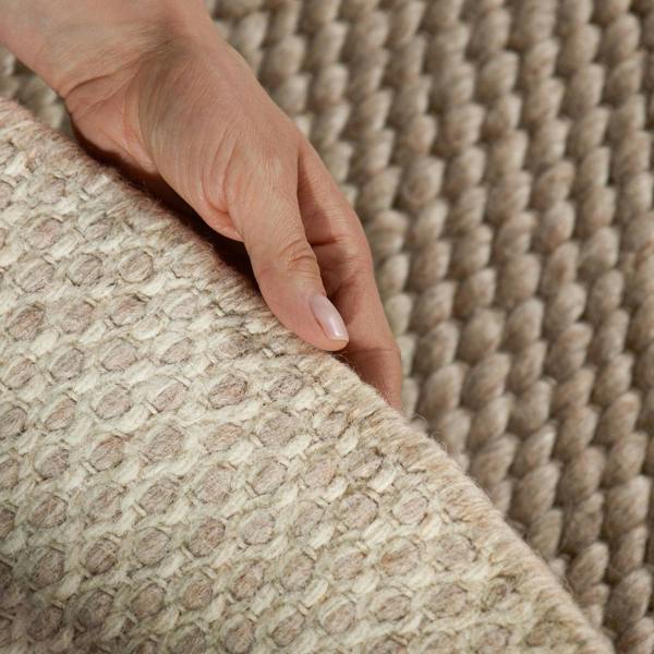 Close-up of a hand touching a textured beige carpet