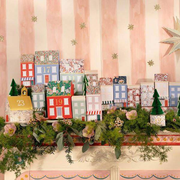 Liberty floral print paper village advent calendar with honeycomb trees and gold foil accents arranged on a festive mantelpiece.