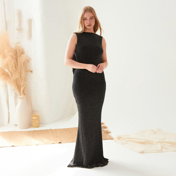 A woman is standing in a room wearing a Sarvin Black Cowl Back Gown.