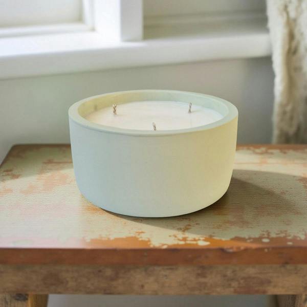 Ceramic candle holder with three candles on a wooden surface near a window.