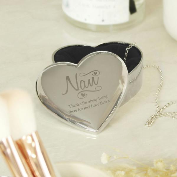A silver heart-shaped trinket box by Abode Home & Gifts, sitting on a white marble dressing table next to makeup brushes. The lid is slid slightly back to reveal the dark lining and an engraved message reading "Thanks for alway being there for me! Love Evie x".