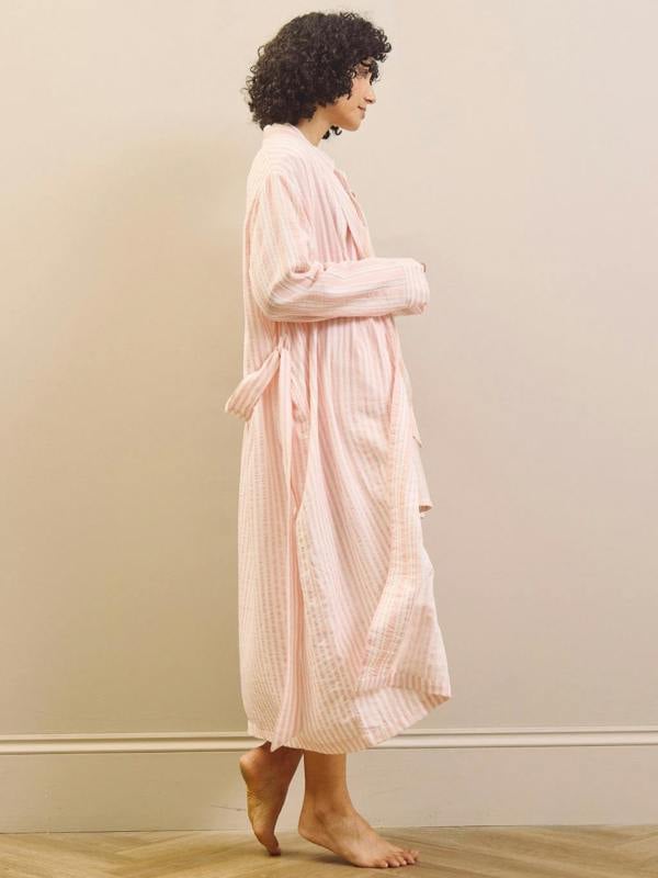 Woman wearing a pink striped pyjama set and robe against a plain background
