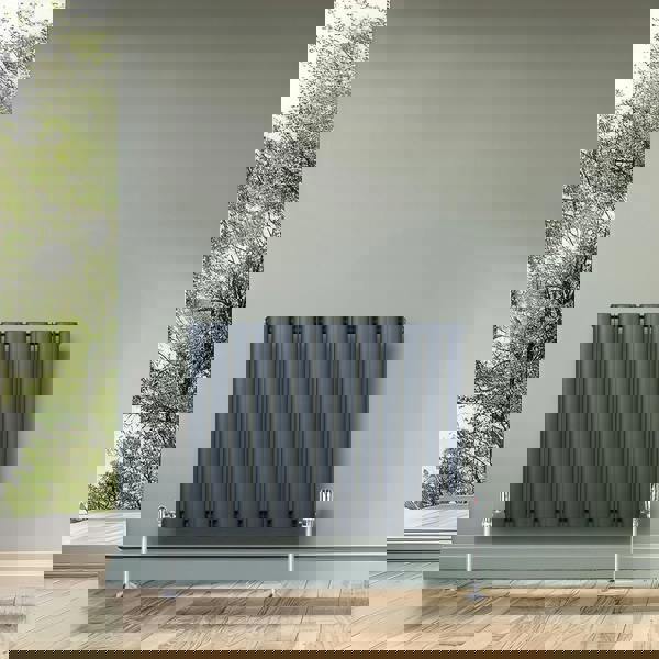 Oval single column radiator in anthracite grey, featuring vertical tubes and chrome valves, mounted on a light green wall