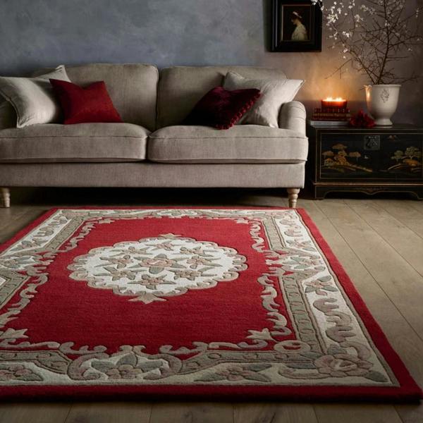 Red patterned rug in a living room with a beige sofa and decorative items.