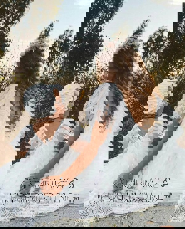 Two young girls in white dresses sitting outdoors with trees in the background.