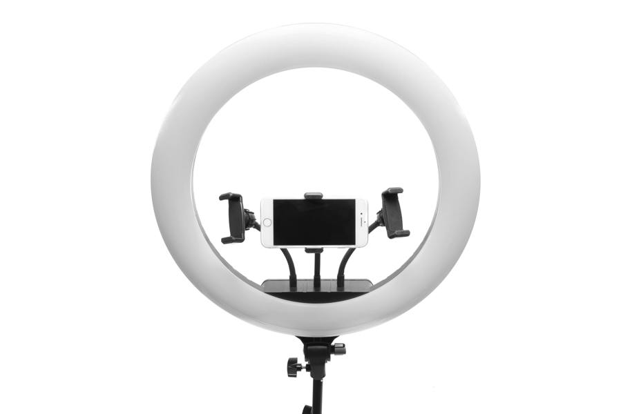 The Rio Professional Makeup & Vlogging 18-inch (45cm) Dimmable LED Ring Light, mounted on a tripod with a smartphone in the center, delivers ideal lighting for flawless makeup application against a white background.
