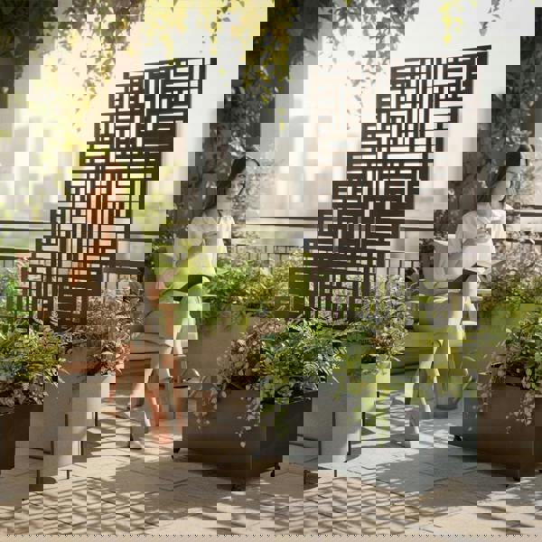 A person relaxing on a balcony reading a book beside a modern metal privacy screen with a built-in planter box filled with lush green plants.