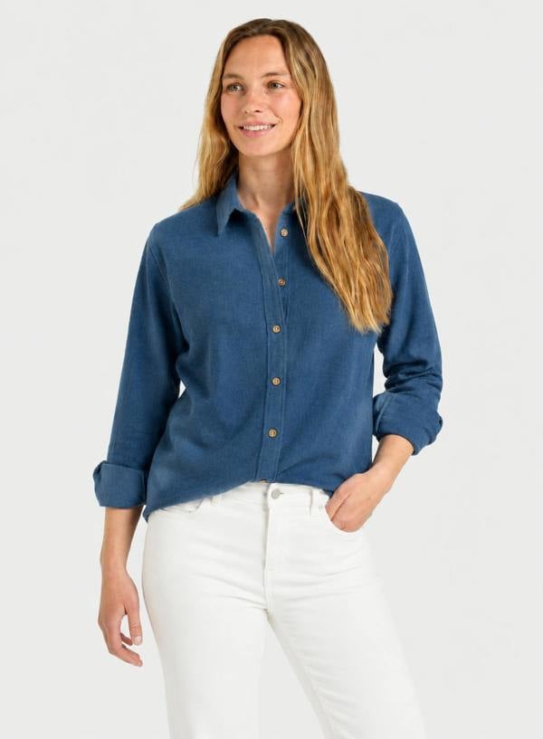 A woman modeling a blue long-sleeve button-up shirt with white pants against a light gray studio background.