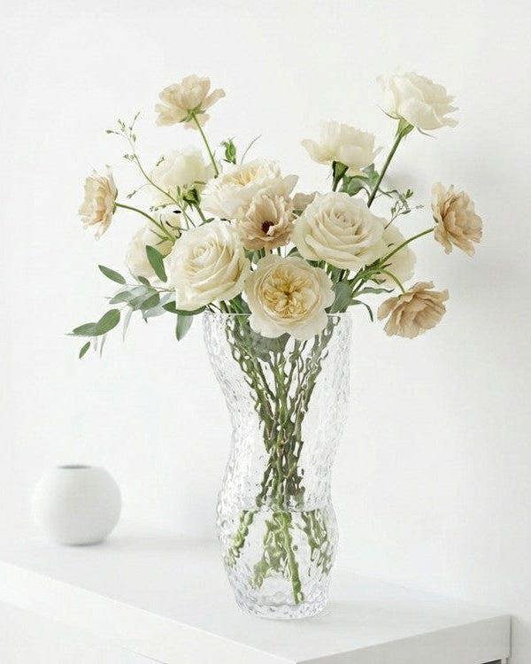 Clear textured vase with white flowers on a wooden surface next to books