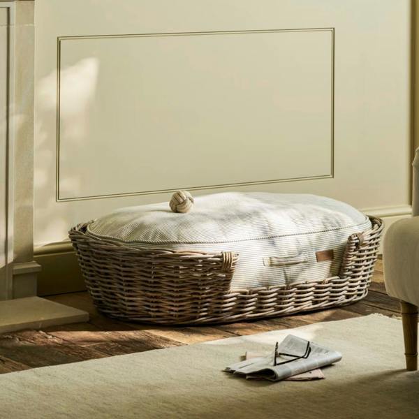Extra Large Hove Rattan Pet Bed with a plush green and cream striped ticking cushion and a toy.