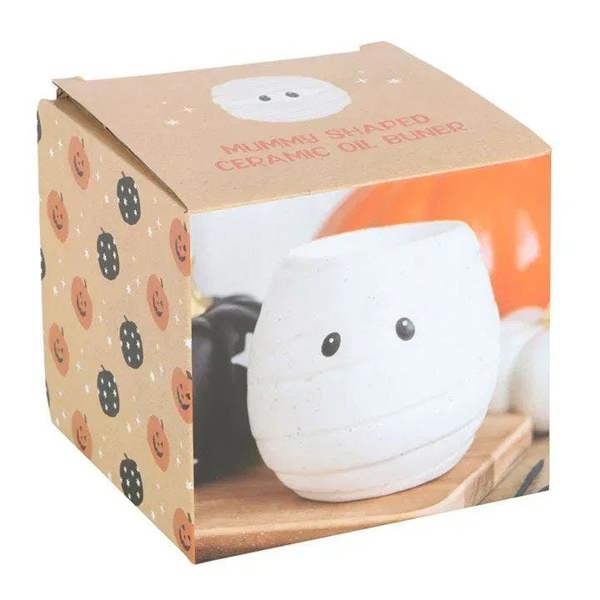 White ceramic mummy-shaped oil burner shown in retail packaging with black dot eyes