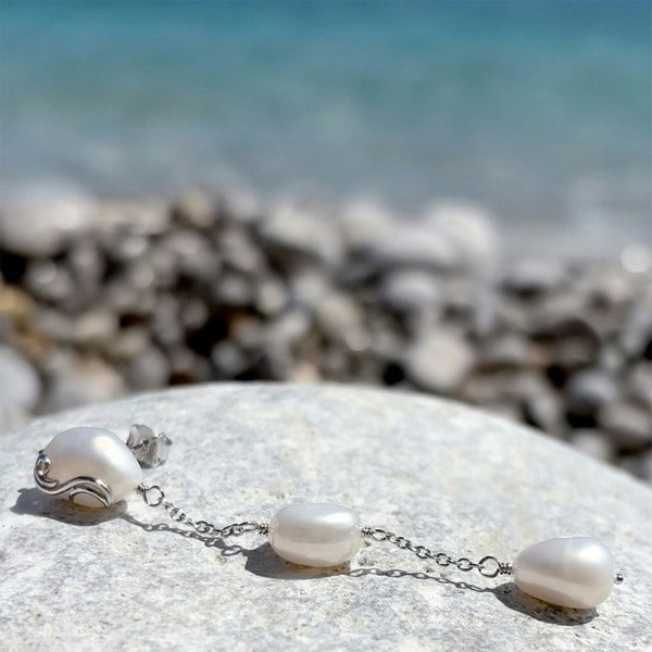 Silver drop earrings with multiple pearls resting on a beach rock.