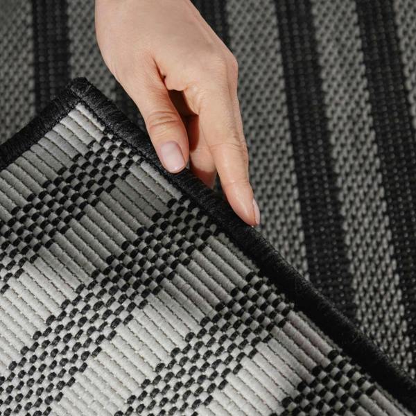 Person's hand touching a textured black and gray rug