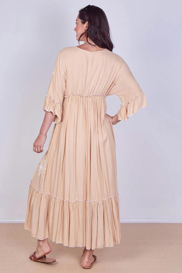 Woman wearing a beige dress with ruffled sleeves and bottom hem on a plain background