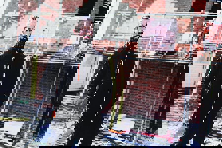 Scruffs Trade Flex Softshell Mens Zip Up Work Warm Jacket Coat, a man wearing a black softshell jacket with zip-up front, in a construction site setting.