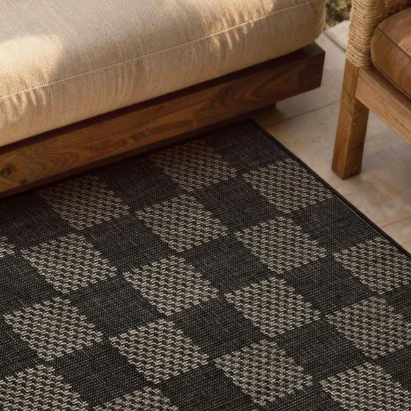 Patterned black and gray rug on a patio with wooden furniture.
