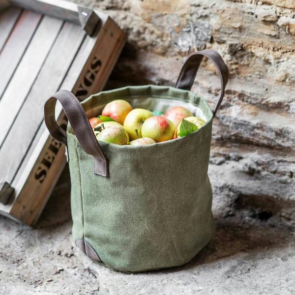 Hidcote green canvas garden storage bag filled with freshly picked apples next to a rustic wooden crate.