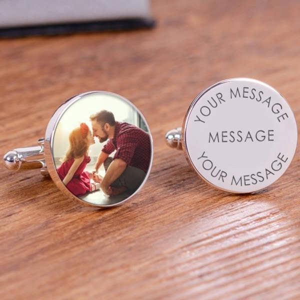 A pair of silver stainless steel cufflinks resting on a wooden surface showing a photo of a dad and daughter on one and text templates on the other.