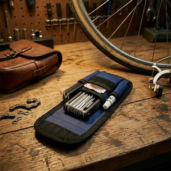 An open blue fabric tool pouch displaying a folding multi-tool and tyre levers on a rustic wooden workshop table next to a bicycle wheel.