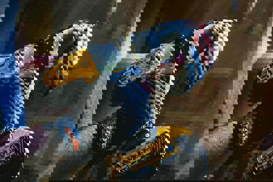 Scruffs Trade Precision Mens Work Padded Palm Gloves, close-up of an individual wearing black and gray gloves while holding a power drill.