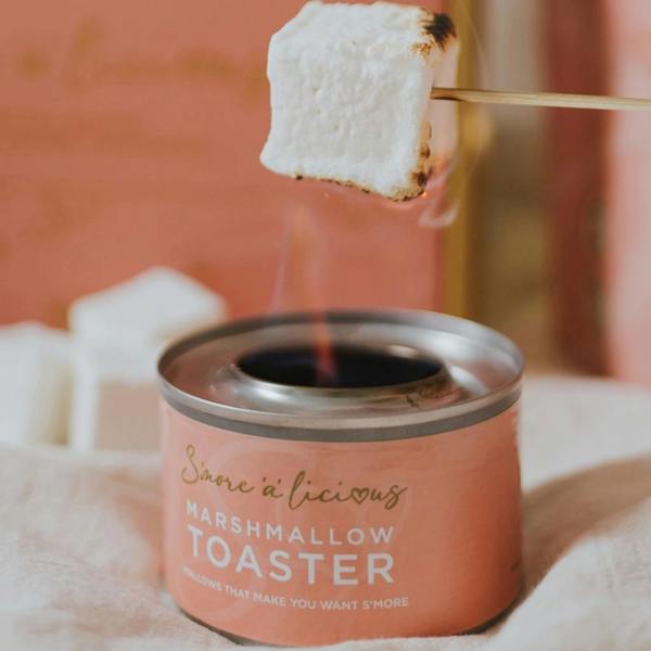 A classic white vanilla marshmallow being toasted on a wooden skewer over a pink S'more 'a licios marshmallow toaster.