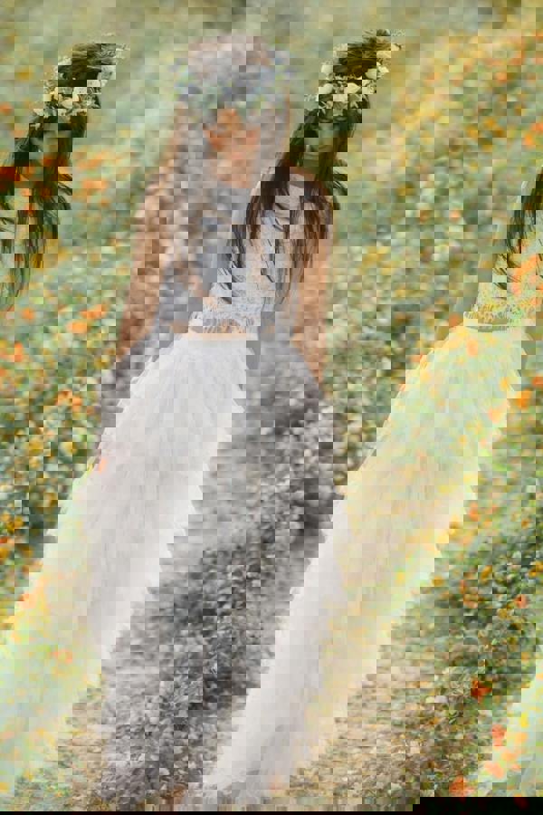 Flower girl in a white dress with a floral crown standing in a field of flowers.